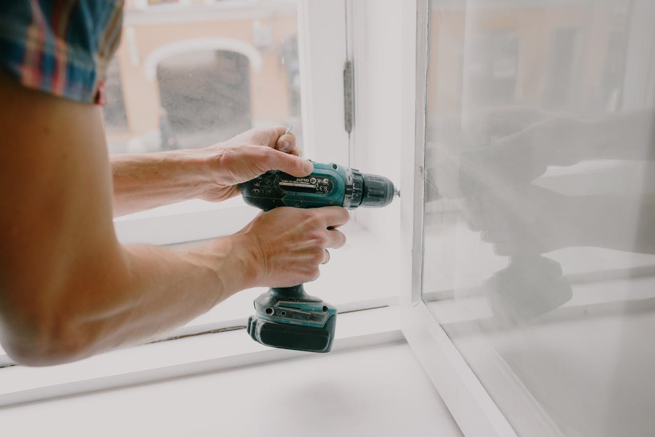 about-01 A person using an electric drill to repair or install a window indoors.